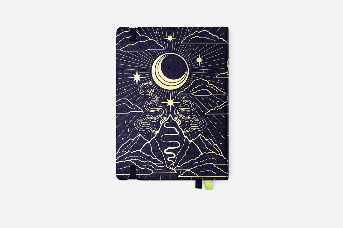 Notebook with celestial design featuring moon, stars, and mountains on a dark blue background.