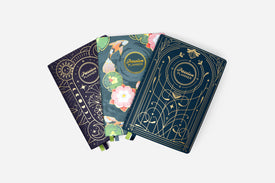 Three decorative planners with floral and celestial designs on a white background