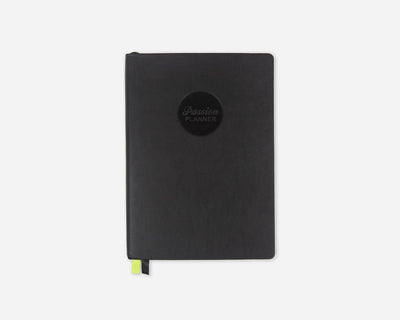 A black faux leather 2027 Passion Planner with a circular black logo on the front and a small lime green ribbon bookmark peeking out from the bottom, set against a plain light gray background.