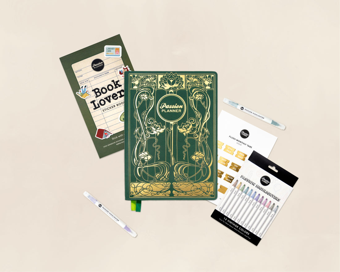 A flat-lay arrangement of themed stationery and art supplies on a light beige background, including a green and gold decorative 2027 planner, a Book Lovers Sticker Book, monthly tabs, and a set of colorful highlighter pens.