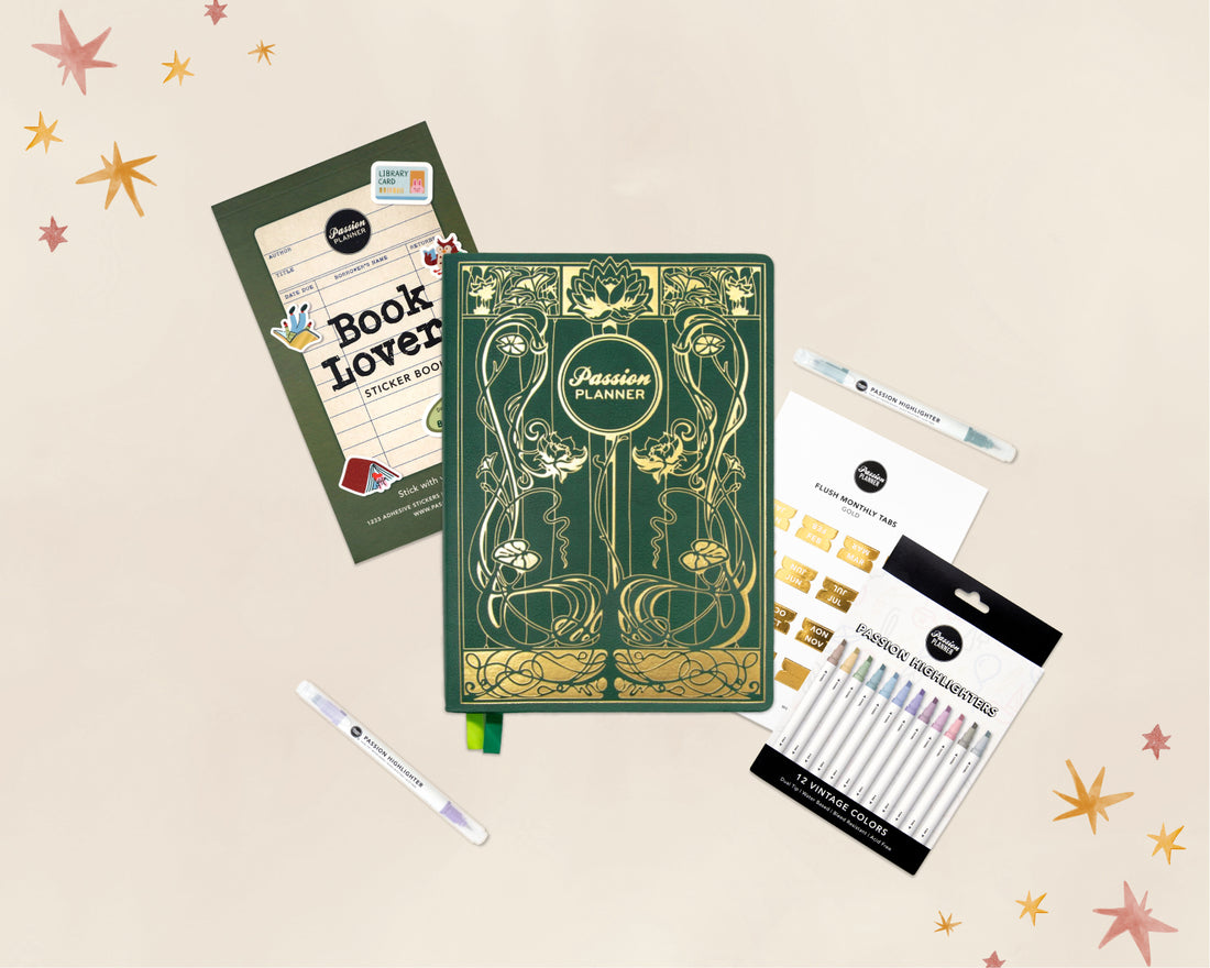 A flat-lay product arrangement on a light beige background with decorative star confetti. The main item is a green 2027 journal with ornate gold Art Nouveau-style illustrations and the title &
