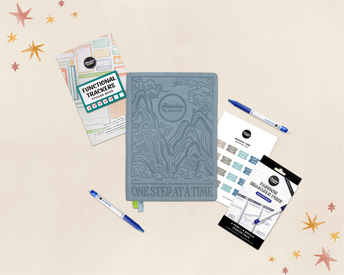 A styled flat-lay of a planner set on a warm cream background with decorative star graphics. The main item is a slate blue embossed 'Passion Planner' journal, surrounded by coordinating accessories including a sheet of functional tracker stickers, blue pens, and monthly tabs.