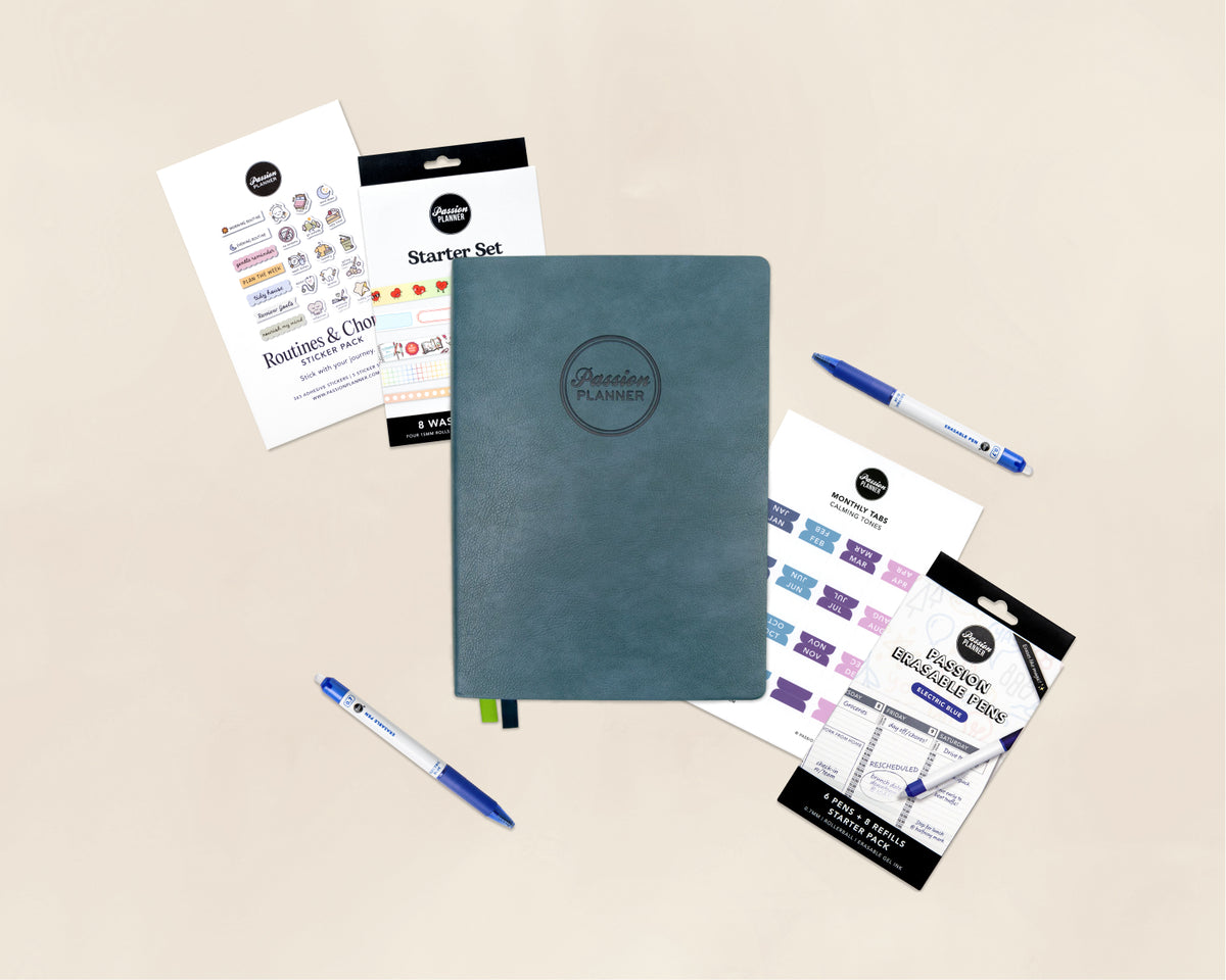 A flat-lay product shot of a planner starter set on a warm beige background. The set includes a dark teal-blue textured hardcover planner with an embossed logo, blue pens, sticker sheets, washi tape, and monthly tab stickers.
