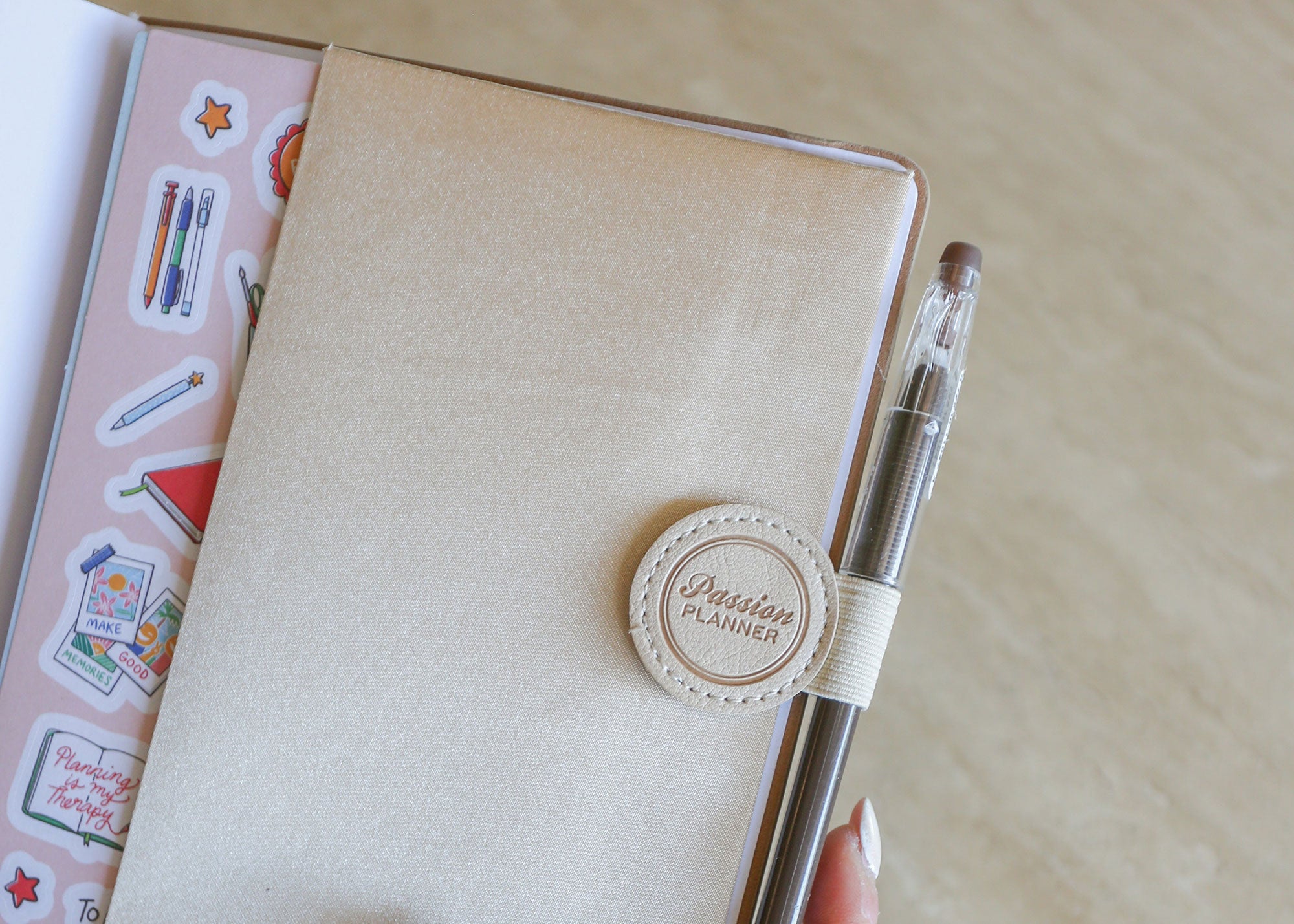 Beige planner with a pen loop and decorative stickers on a wooden desk