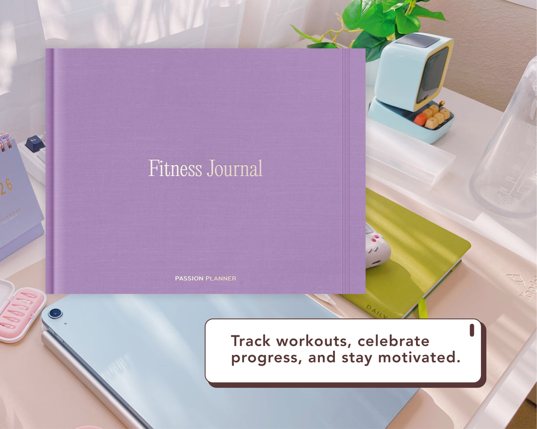 A purple Fitness Journal by Passion Planner is displayed on a desk with a tablet, notebook, and small retro TV prop. A text bubble reads: &