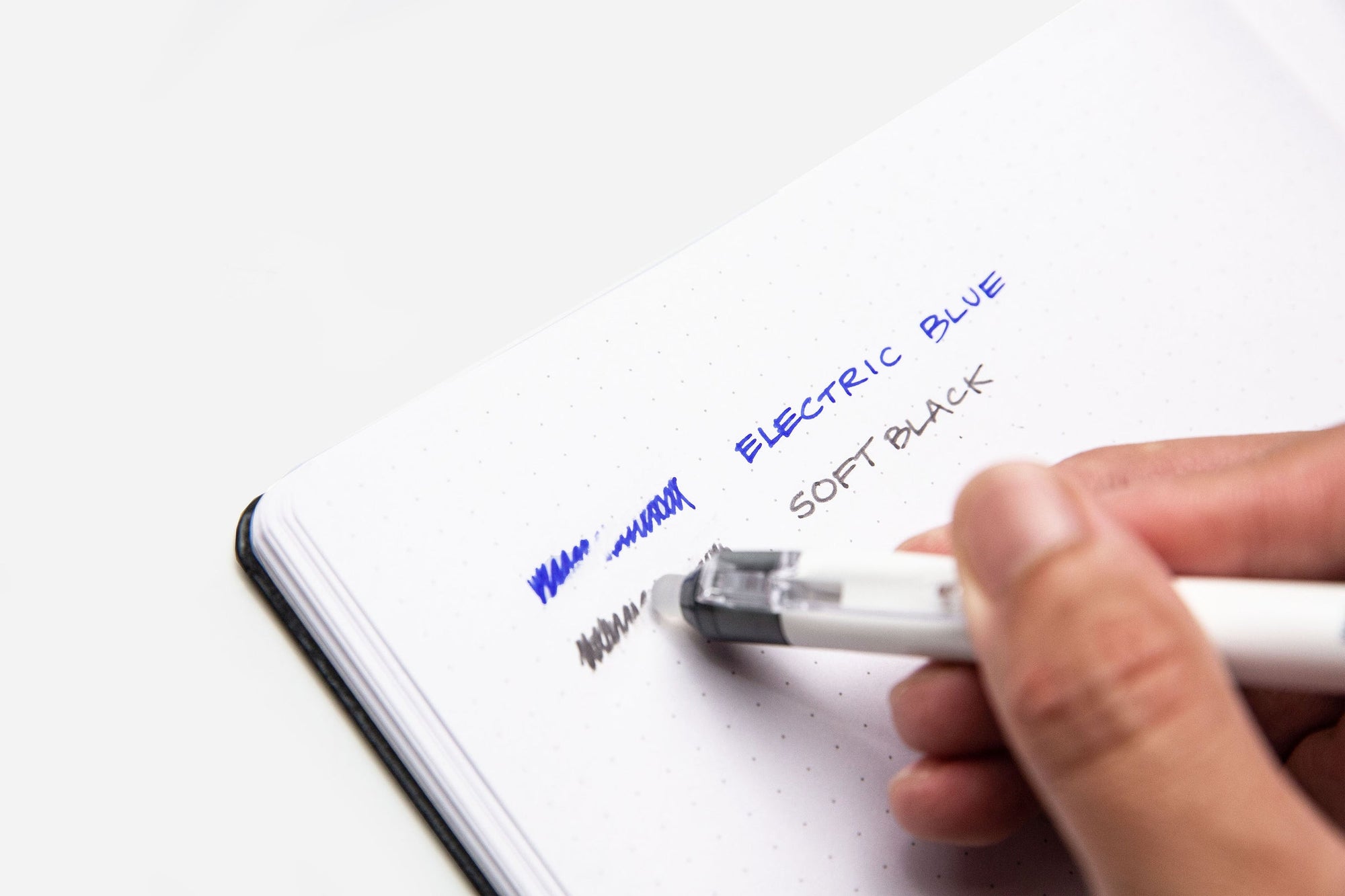 Electric Blue and Soft Black written in a notebook and being erased by a pen
