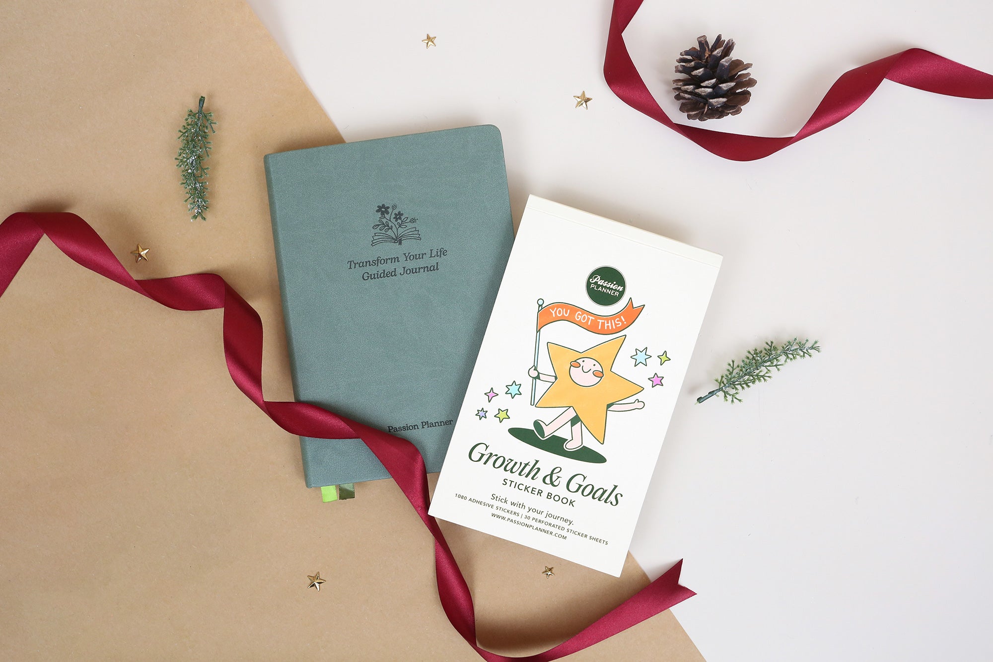 'Transform your life' guided journal and a 'Growth & Goals' sticker book on a textured surface with ribbons and pine cones.