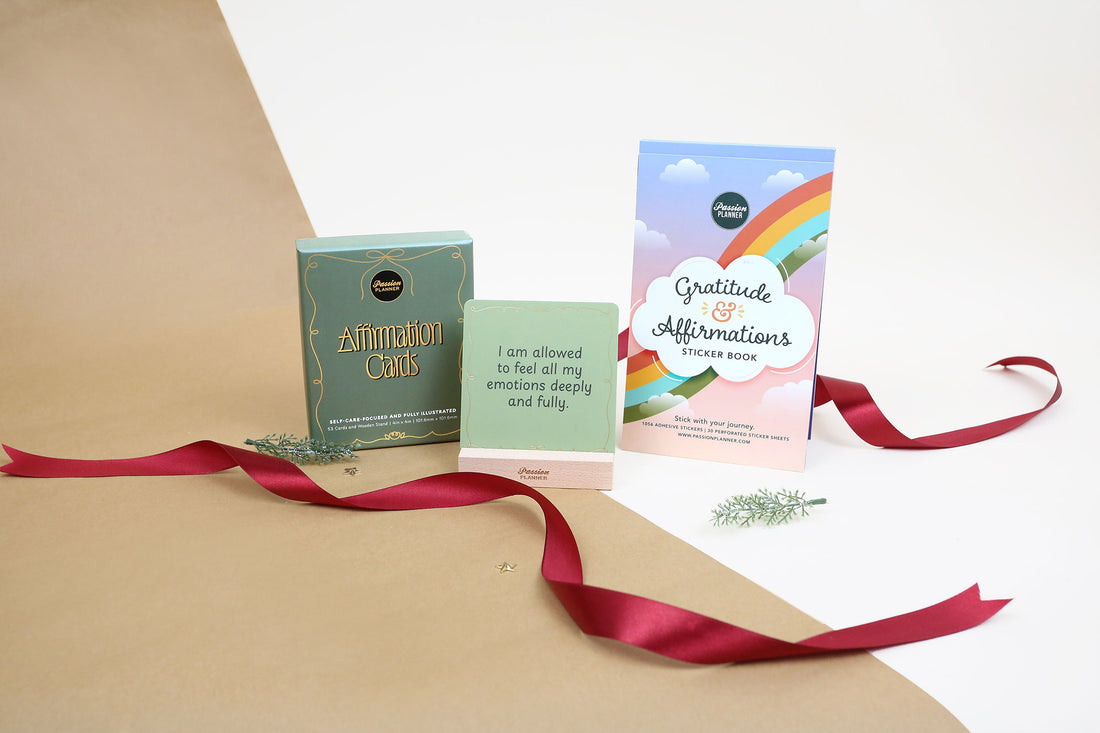 Set of affirmation cards and a gratitude and affirmations sticker book with ribbon and a white and brown background. 