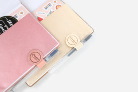 Pink and beige planners with faux leather pen loops on a white surface