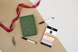 Green daily notebook, pen, and patterned washi tape set on a beige surface with a red ribbon.