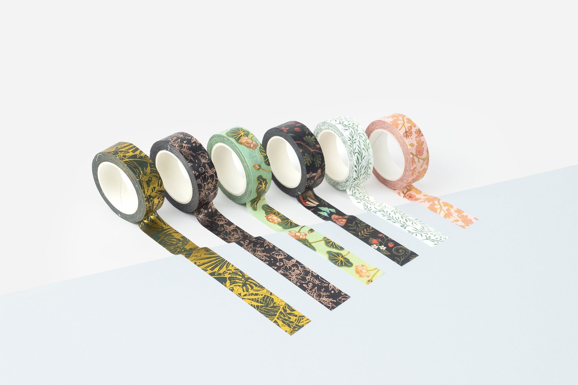Six rolls of decorative washi tape expanded on a white background